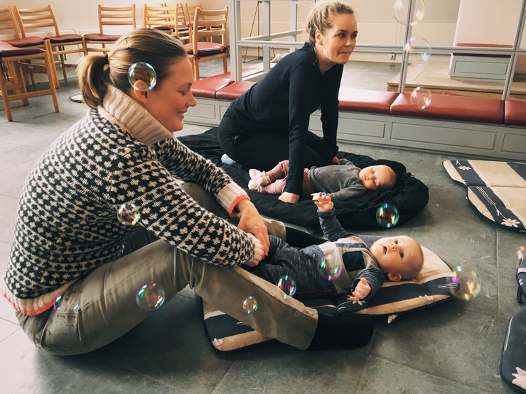 Sæbebobler omkring to kvinder, der sidder på gulv - deres babyer ligger foran dem.