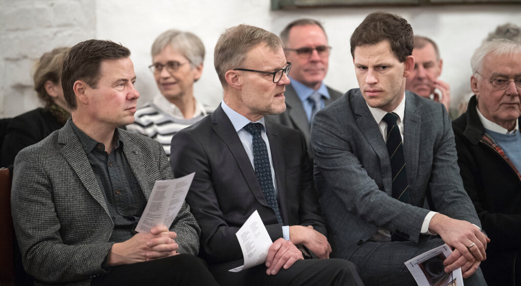 Tre mænd i jakkesæt sidder ved siden af hinanden