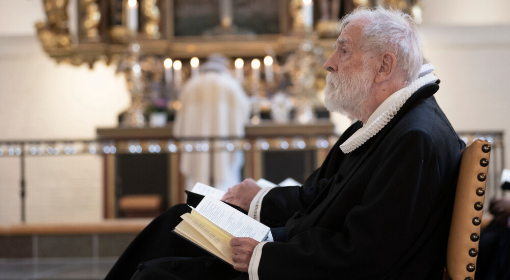 Mandlig præst sidder på stol med salmebog åben